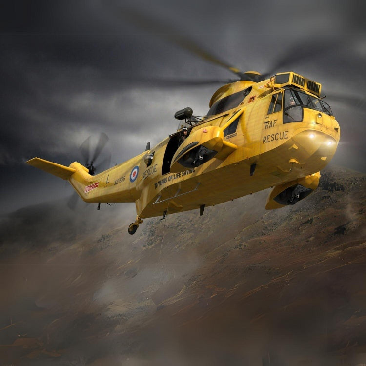 Yellow Sea King helicopter in flight with a mountainside and dark sky behind.