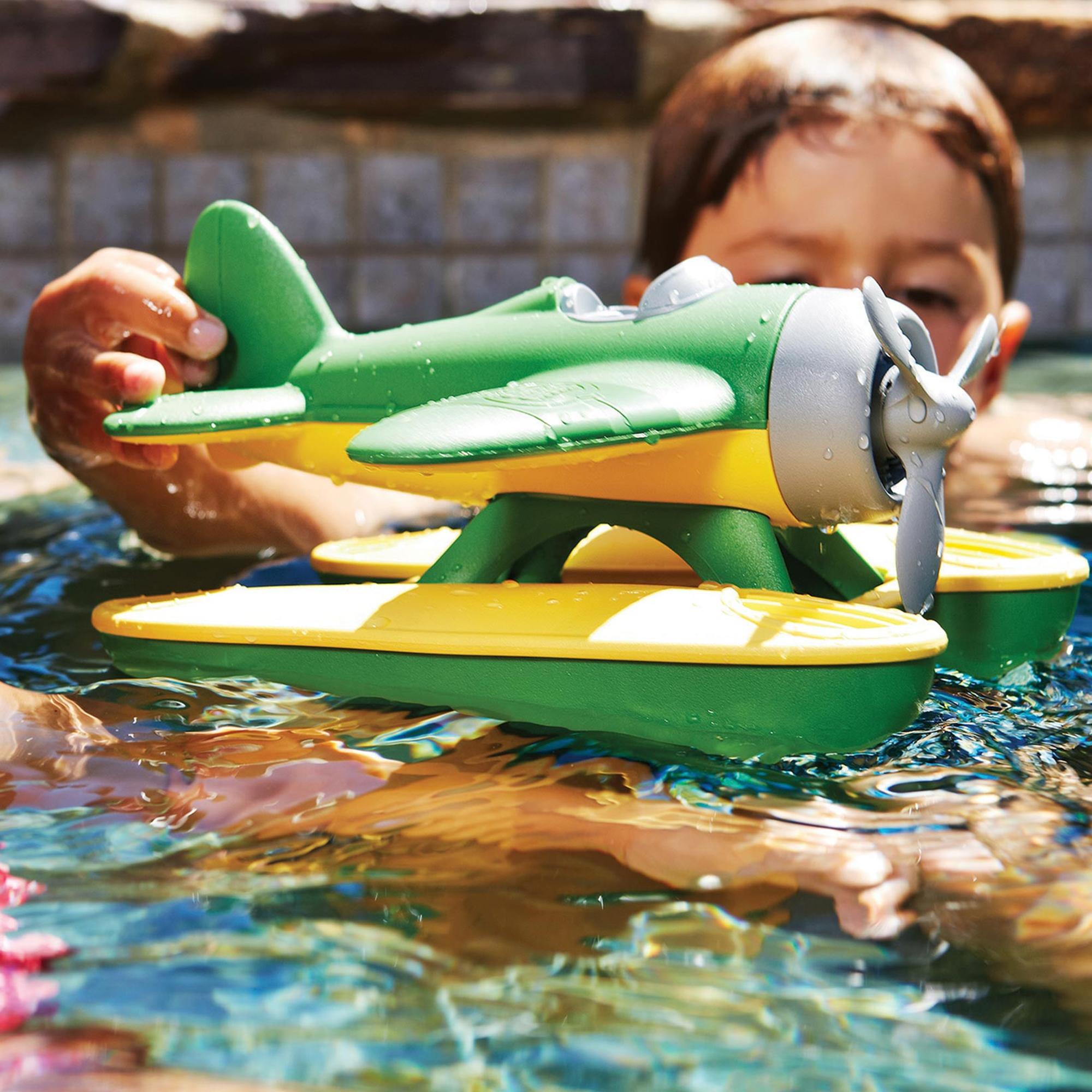 Boy playing with green and yellow seaplane as it floats on water.