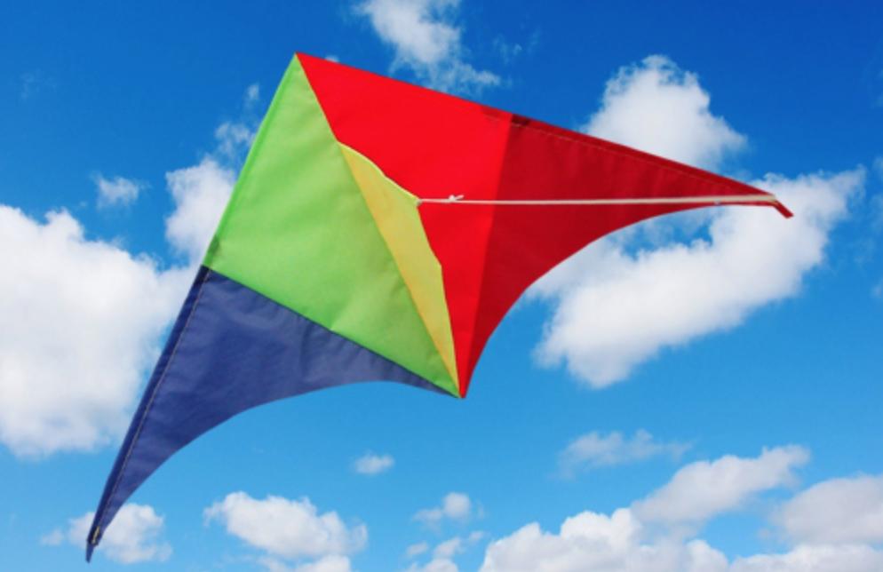 Rainbow coloured Delta kite with blue sky and clouds behind.
