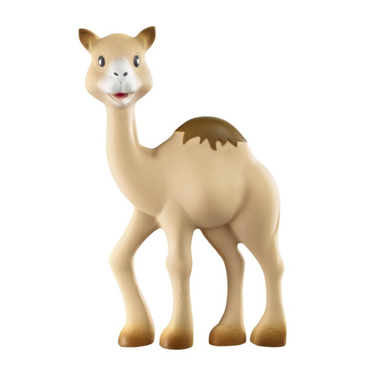 Al' Thir the Companion by Sophie La Giraffe is a toy camel figure standing upright, featuring a smiling expression. Made from natural rubber, it offers teething relief for babies. The beige color with darker patches on its hump and feet adds visual interest against a plain white background.