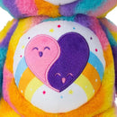 Close-up of the Care Bears Eco-friendly Friends Forever (35cm) by Basic Fun, a vibrant plush toy with a rainbow pattern and an embroidered belly design featuring overlapping pink and purple hearts surrounded by small stars and a rainbow.