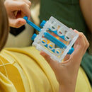 A person in a yellow shirt holds the Criss Cross Cube by Smart Games, a transparent puzzle filled with blue rods and yellow rings, ideal for enhancing problem-solving skills and exploring logic games.