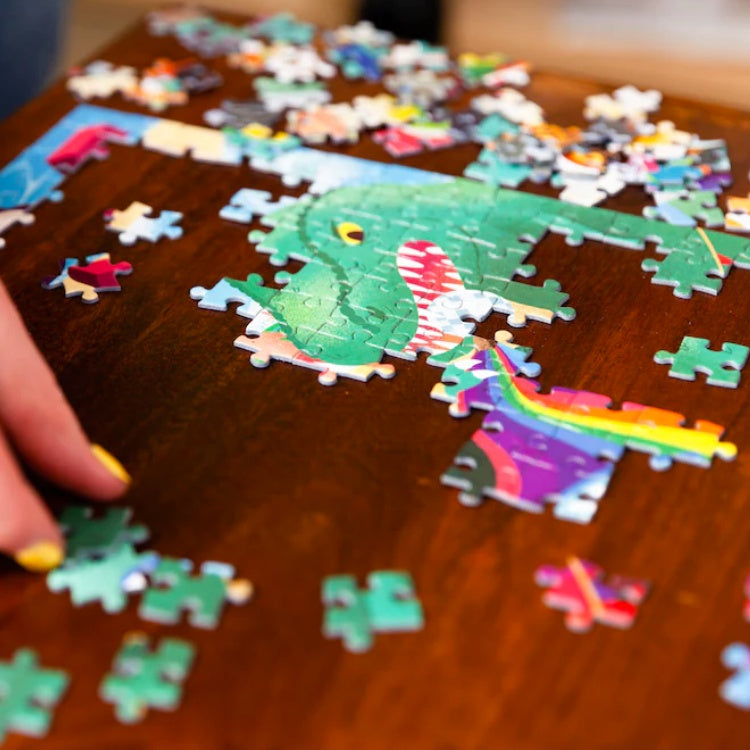 Close up of someone putting the jigsaw puzzle pieces together on a brown wooden table.