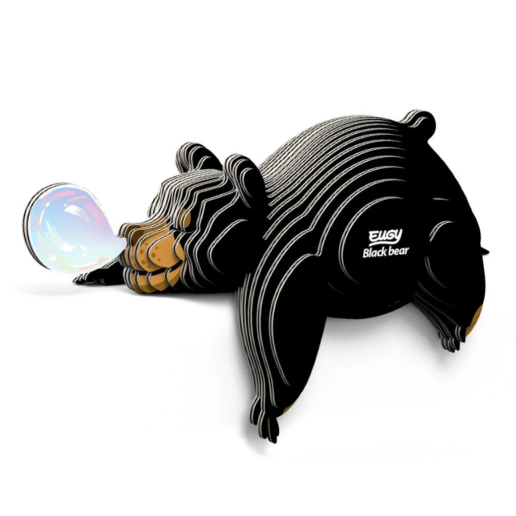 A stylized, striped Eugy Black Bear puzzle by EUGY is playfully blowing a shiny, colorful bubble while lying down. "Eugy Black Bear" appears on its side, set against a white background—ideal for educational decor.