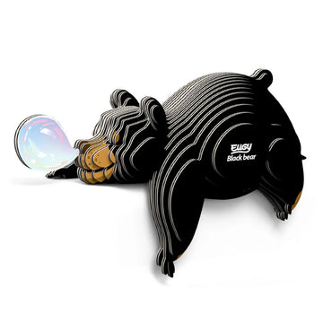 A stylized, striped Eugy Black Bear puzzle by EUGY is playfully blowing a shiny, colorful bubble while lying down. "Eugy Black Bear" appears on its side, set against a white background—ideal for educational decor.