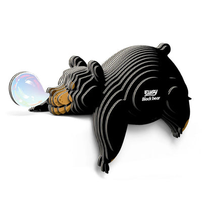 A stylized, striped Eugy Black Bear puzzle by EUGY is playfully blowing a shiny, colorful bubble while lying down. "Eugy Black Bear" appears on its side, set against a white background—ideal for educational decor.