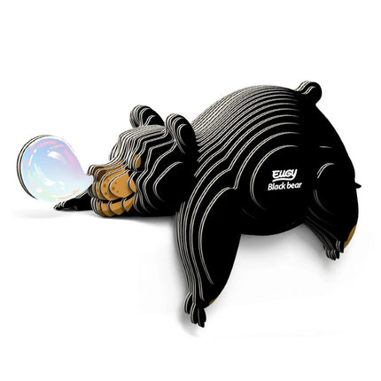 A stylized, striped Eugy Black Bear puzzle by EUGY is playfully blowing a shiny, colorful bubble while lying down. "Eugy Black Bear" appears on its side, set against a white background—ideal for educational decor.