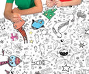 Two children in red and green shirts eagerly lean over an Eggnog Christmas Colour-In Giant Poster / Tablecloth, filled with whimsical, unfinished drawings of animals, gifts, and stars. They point excitedly at the poster, planning their next creative strokes.