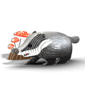 The EUGY Badger, a stylized, cartoonish figurine crafted from sustainable materials, stands beside red and white mushrooms on a plain white background. As part of the EUGY toy figures collection, it features "Busy Badger" on its side with distinct black, white, and gray stripes.