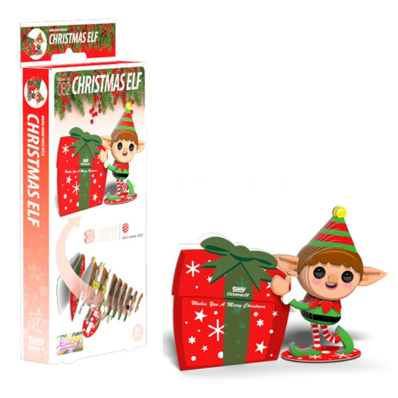 The Eugy Christmas Elf figurine, crafted from eco-friendly materials, features a cheerful expression and stands beside a large red gift box with green accents. The charming holiday packaging highlights the elf and box with "Christmas Elf" in bold red letters, perfectly embodying the spirit of EUGY toy figures.