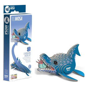 A 3D cardboard model kit of a prehistoric marine predator, the Mosasaurus, called the EUGY Mosa by EUGY, is displayed. The image shows the blue-bodied, sharp-toothed model on the right and its eco-friendly packaging on the left, featuring an illustration of the creature with product details.