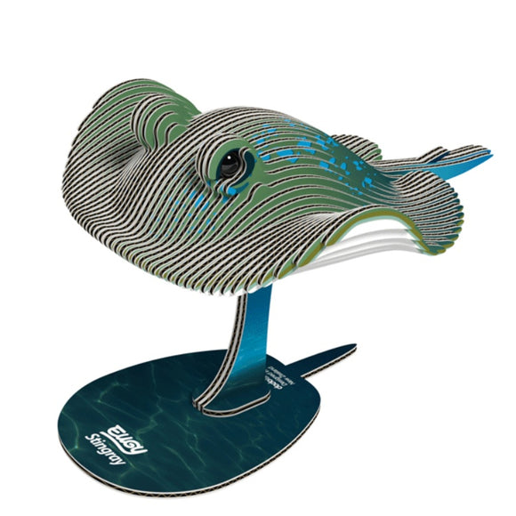 Introducing the EUGY Stingray, a 3D masterpiece crafted from sustainable cardboard layers. It features a stylized depiction with shades of green, blue, and white on a blue circular base. Proudly echoing eco-friendliness, it embodies the "EUGY" brand and "Stingray" essence.