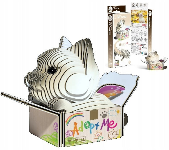 The Eugy Cat - Mocha 3D cardboard puzzle from EUGY features a cat lounging in a box with colorful designs and the words "Adopt Me." This eco-friendly kit, rich in creativity, includes packaging with step-by-step assembly instructions and vivid images.