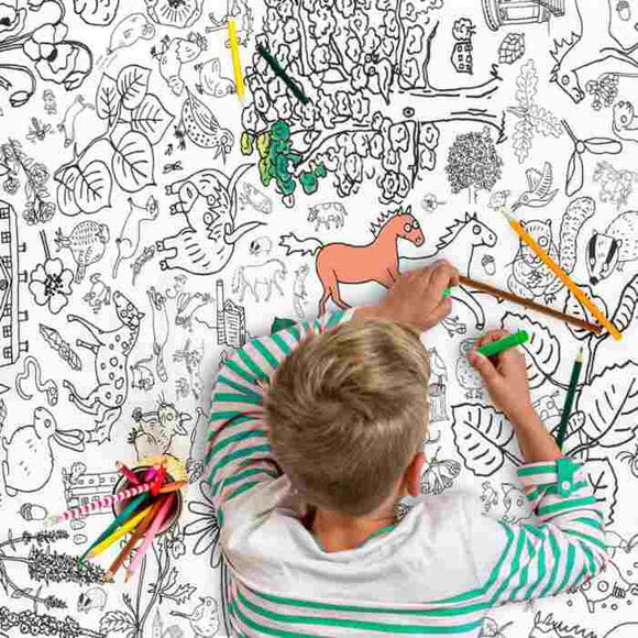 A child with blond hair and a striped shirt colors with markers on an eggnogg Giant Poster/Tablecloth – Countryside, featuring outlined illustrations of plants, animals, and shapes. A horse is partially colored in orange and green, while colored pencils nearby await more fun coloring activities.