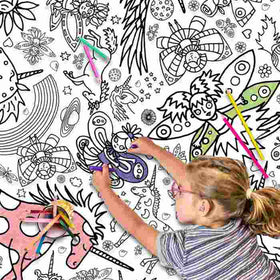 A child with glasses focuses on coloring a Giant Poster/Tablecloth by eggnogg, featuring whimsical unicorns and fairies. Vibrant colors bring the scene to life as colored pencils lay scattered around.