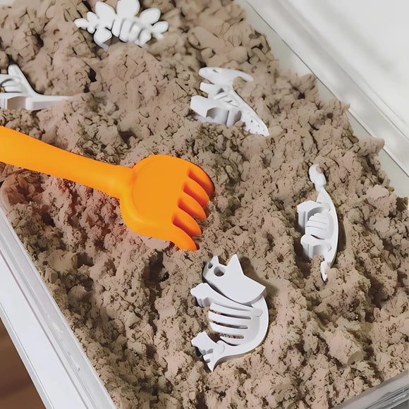 Play sand with white dinosaur skeleton toys and an orange rake in a container