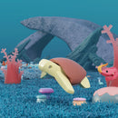 A 3D-rendered underwater scene features a Halftoys Diorama - Green Turtle swimming among vibrant coral, mushrooms, and plants with large rocks behind it and a pink seahorse to the right in this ocean-themed playset by Halftoys.