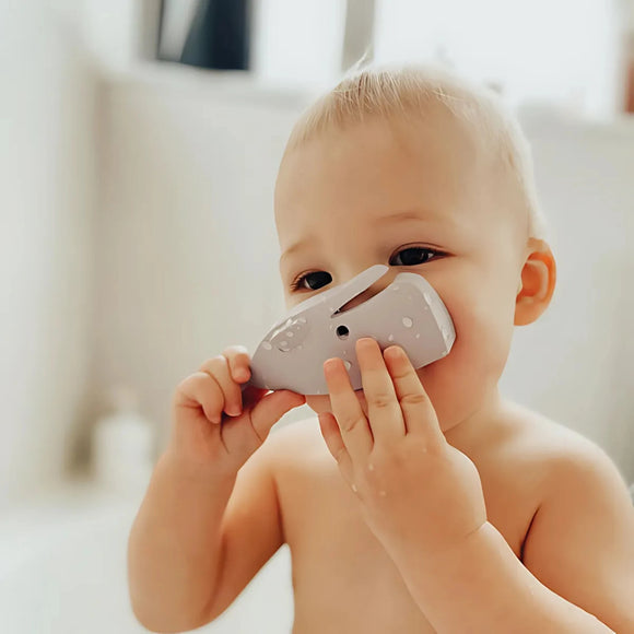 A baby holds a Halftoys Picture Book - Sperm Whale by Halftoys up to their mouth, gazing upwards in a soft-focus bathroom setting—ideal for introducing educational sea animal toys.