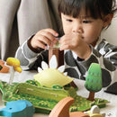 A young child in a patterned shirt carefully plays with the Halftoys Diorama - Stego by Halftoys, an educational dinosaur toy and tree puzzle set that encourages interactive STEM learning.