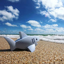 A Halftoys Diorama - White Shark by Halftoys rests on a sandy beach near gentle waves, beneath a bright blue sky with scattered clouds.