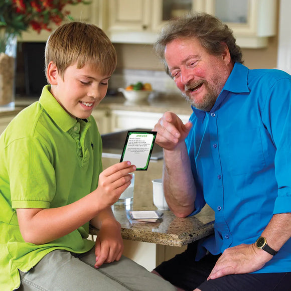 A boy and an older man sit smiling at a kitchen counter as they enjoy Outset Media’s MindTrap Cards Left Brain Right Brain, bonding over challenging puzzles and questions for a fun brain workout with cards, coffee, and laughter.