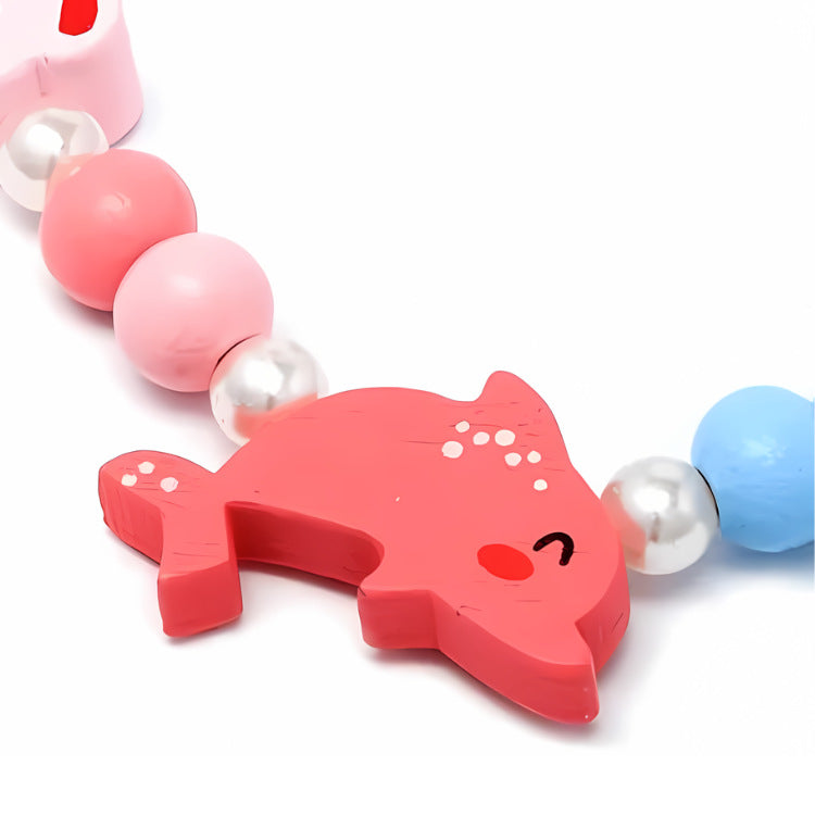 The Dolphin Bead Necklace & Bracelet Set by molly & rose features a playful pink shark-shaped charm with a smile, adorned with small white dots. The bracelet boasts alternating beads in pink, white, and blue hues for a whimsical touch.