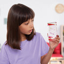 A young girl with brown hair, in a purple shirt, curiously observes a Sensory Motion Bubbler Stair filled with colorful floating shapes. The softly blurred room interior adds to the stress-relief ambiance.