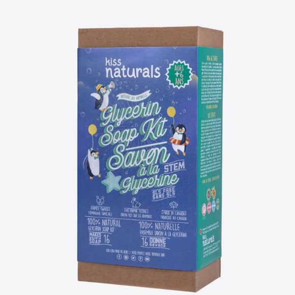 A rectangular box of the DIY Natural Glycerin Soap Kit by KISS NATURALS. The green packaging showcases vibrant illustrations of penguins and bubbles on the front. It emphasizes that the product is made with all-natural ingredients, suitable for ages 6 and up, with information available in both English and French.