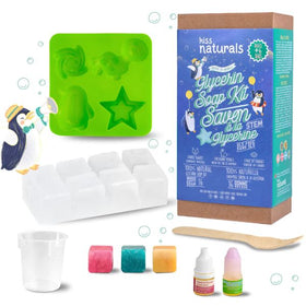 The DIY Natural Glycerin Soap Kit by KISS NATURALS includes a green silicone mold with various shapes, white soap blocks, three colorful soap samples, a small measuring cup, a wooden stick, and two bottles of coloring or scent. The packaging prominently displays the brand and product information.