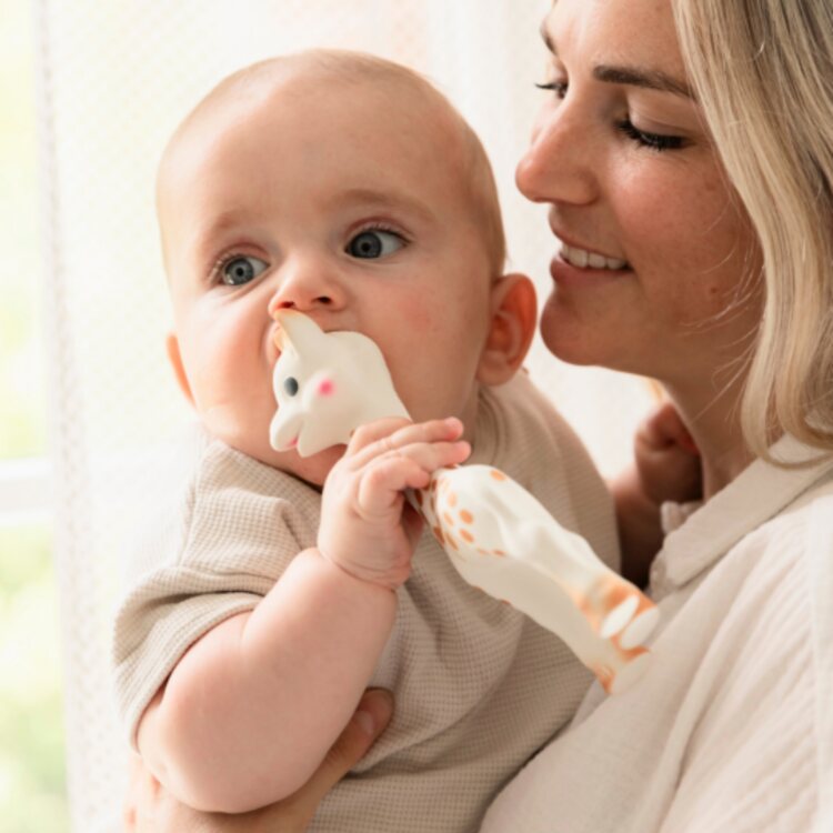 Blonde woman holding a baby who's using a giraffe-shaped teething toy.