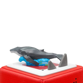 A toy model from Tonies, "Tonie - National Geographic Kids - Whale," features a humpback whale swimming on a vibrant red base adorned with the National Geographic Kids logo, capturing the spirit of an ocean adventure alongside two gray fin-like shapes.