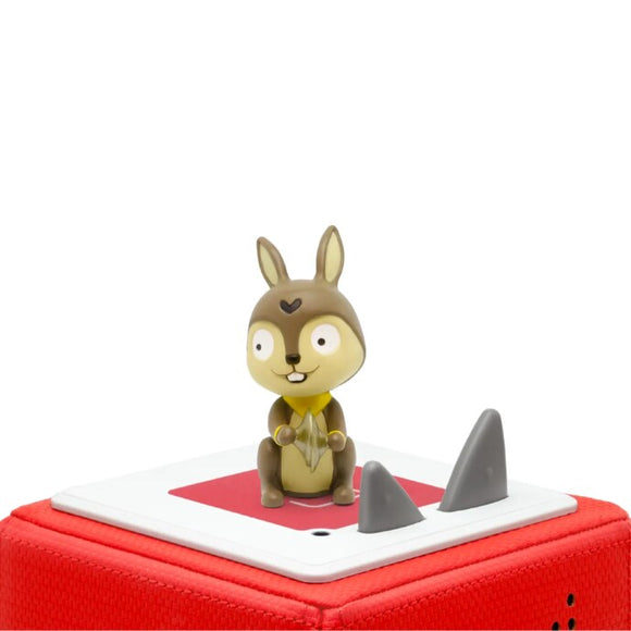 A small figurine of a cartoonish squirrel with large eyes and a heart on its forehead sits atop a red and white Toniebox speaker, featuring the "Tonie - Favourite Children’s Songs – Sing-a-long Songs" collection by Tonies. The speaker, ideal for nursery rhymes or children's songs, has a triangular gray volume control. The background is plain white.