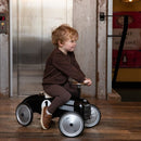Young boy in a brown outfit riding a black metal car with silver wheels.
