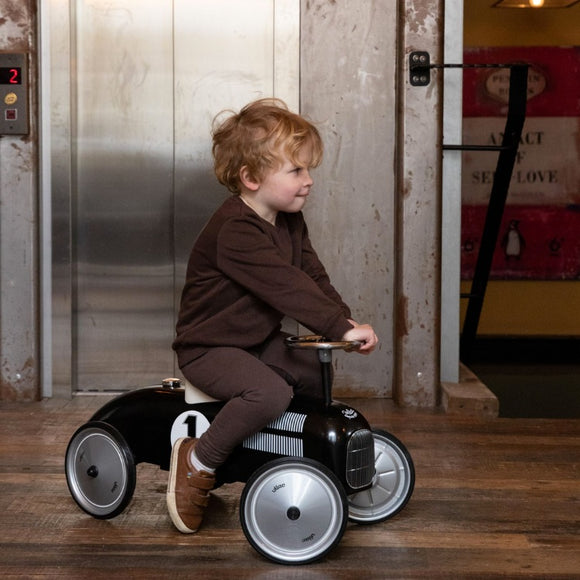 Young boy in a brown outfit riding a black metal car with silver wheels.