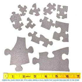 Cobble Hill's "Call of the Wild" 350-piece Family jigsaw puzzle features various pieces in different sizes above a yellow measuring tape marked with inches, showcasing large, medium, and small pieces cascading from one side to the other.