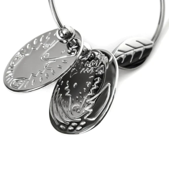 A close-up of silver jewelry reveals a bracelet with three charms: two engraved round discs and a small leaf. The polished finish reflects light, echoing the elegant style of YUMMIKEYS' stainless steel Woodland Teething Keys.