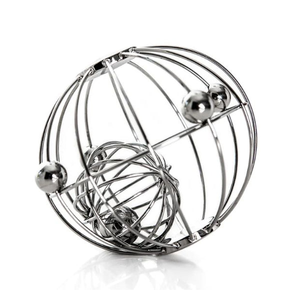 The Yummikeys - Yummirattle by YUMMIKEYS is a stainless steel rattle featuring multiple spherical beads and intersecting wires that form a sphere. Its design aids motor skills development and casts intricate shadows on a white surface.