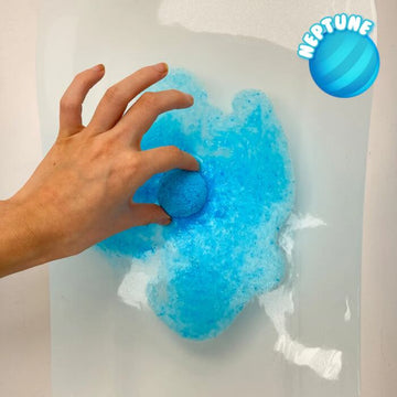 A hand holds a blue bath bomb partly in water, releasing blue fizz. A round "NEPTUNE" logo is in the top right corner, making bath time fun and educational with Baff Bombz Solar System by Zimpli Kids.
