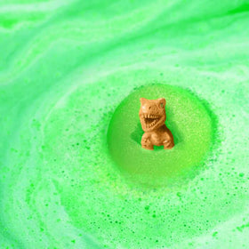 The Zimpli Dino Surprise Figure Baff Bombz by Zimpli Kids reveals a small, child-friendly toy dinosaur amid vibrant green foam, crafted by bubbling bath bombs for a whimsical and playful scene.