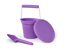 The Toy Shop's Eco Spade set features a purple wheat-fibre toy bucket with a handle, accompanied by a matching lid and eco-friendly spade, all against a plain white background.