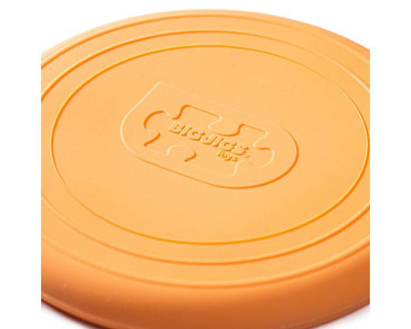 Close-up of an orange silicone Foldable Flyers from The Toy Shop with concentric circles and a puzzle piece embossed in the center. Featuring a matte finish, this sustainable and eco-friendly toy is ideal for environmentally conscious fun.