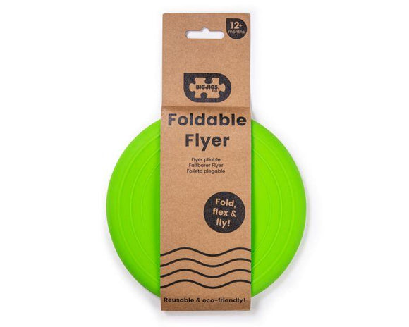 The Toy Shop's Foldable Flyers, a bright green foldable flying disc for ages 12 months and up, is crafted from eco-friendly materials. Partially visible in its cardboard packaging, it features "Fold, flex & fly!" on the front to emphasize its reusability.