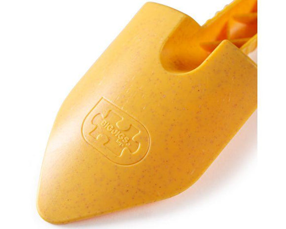 Close-up of a yellow Eco Spade by The Toy Shop, featuring a textured handle. This eco-friendly toy spade has an embossed logo with a puzzle piece and "Diggers USA." Made partly from wheat fiber, it displays light speckles on its surface.