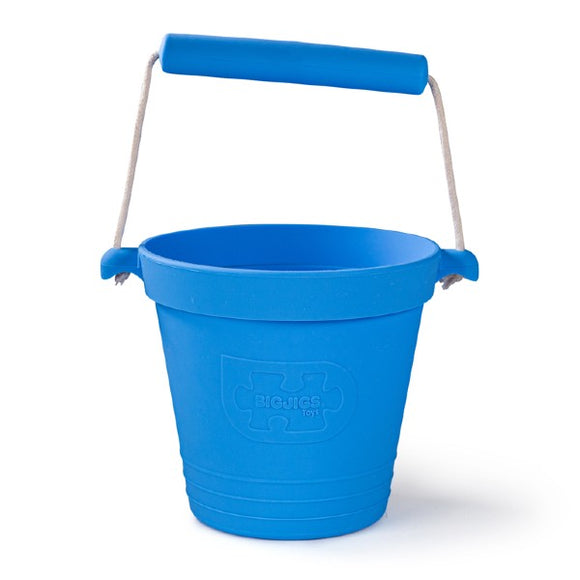 The BIGJIGS Foldable Activity Bucket in ocean blue, made from food-grade silicone with a jigsaw logo and a blue handle with white string, offers an eco-friendly and sustainable toy option for children's play.
