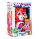 The Care Bears Eco-friendly Flower Power Bear - 35cm by Basic Fun comes in vibrant eco-friendly packaging, showcasing its smiling face and multicolored fur, adorned with cheerful heart-shaped flower illustrations.