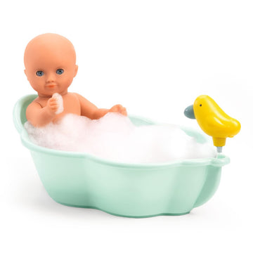 The Djeco Doll Bathtub features a baby doll with blue eyes and no hair sitting in a mint green tub filled with white bubbles. A yellow squirt toy duck attached to the side resembles a faucet, and the doll is holding up an arm.