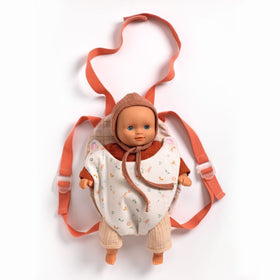 A Djeco Baby Carrier Lavender is securing a baby doll dressed in a brown hood and beige pants. This accessory by Djeco includes adjustable pinkish-orange straps, ideal for carrying. The doll, which has a neutral expression, is positioned on a clean, white background.