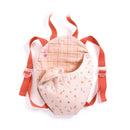 The Djeco Baby Carrier Lavender is a small, backpack-style accessory ideal for dolls. It features vibrant orange adjustable straps and a light pink grid pattern on the top fabric, complemented by a floral design with carrots, leaves, and flowers on a white background at the bottom.