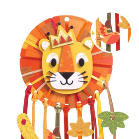 The Djeco DIY Lion Dreamcatcher features a vibrant stylized lion face with a crown, surrounded by a colorful mane. Ribbons adorned with leaf and flower decorations hang below, while an inset displays a bird and leaf design.