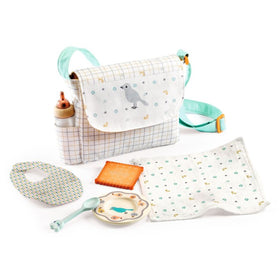 The Djeco Doll Mealtime Set by Djeco includes an adjustable handle bag with a bird illustration, a baby bottle, bib, soft blanket, spoon, plate, and a cookie-shaped toy. Each item features pastel colors and playful designs to delight your little one.